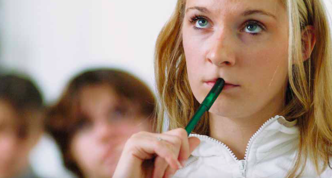 Foto von einer Schülerin, die mit dem Stift am Mund nachdenkt.