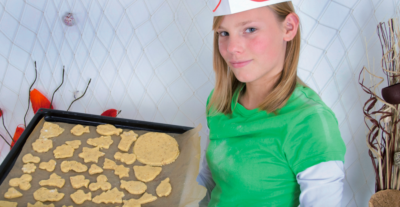 Mädchen als Bäckerin, die ein Blech mit Plätzchen in die Kamera hält.